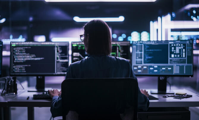 Woman sitting at a computer desk in front of three monitors