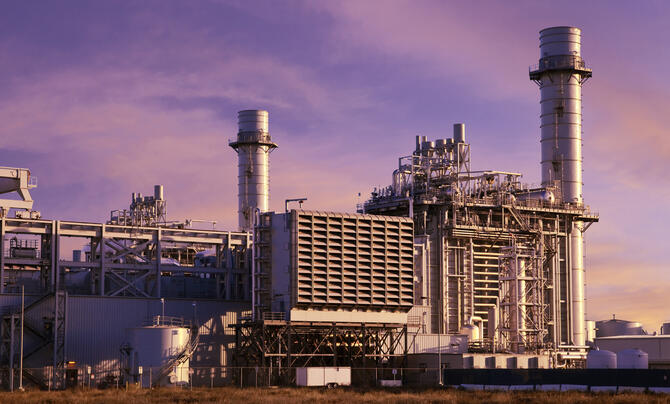 Industrial power plant with tall exhaust stacks, cooling equipment and interconnected pipes against a purple and pink sunset sky.
