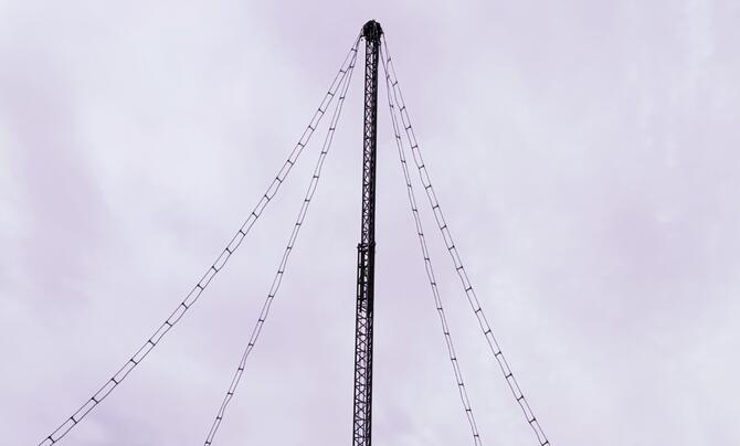 The top part of a thin lattice-type metal tower with four wire lines leading to the very top - this is ALPS (Army Long-Range Persistent Surveillance) system is a passive, long-range aerial surveillance sensor developed by Leidos