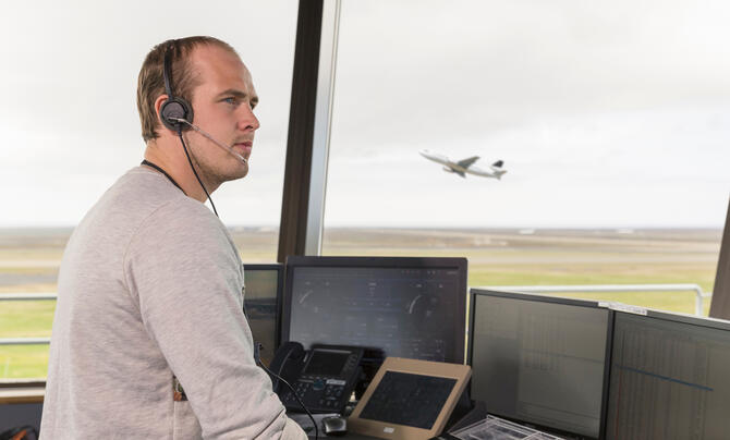 Side view of young man in air traffic control tower, looking away, airplane taking off behind