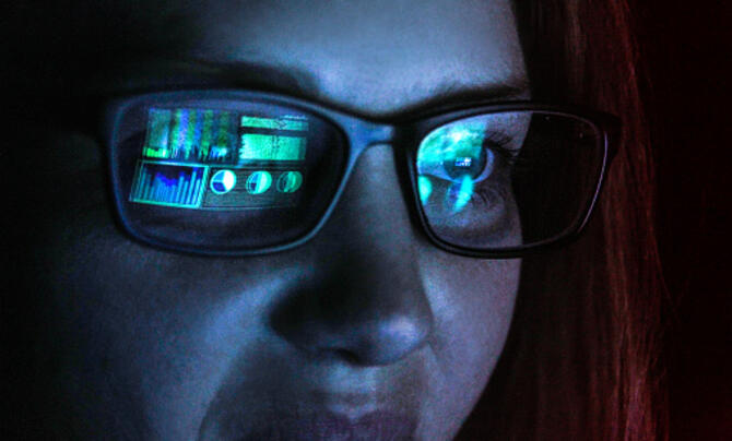 woman in dark room with graphs on computer screen reflecting on her glasses