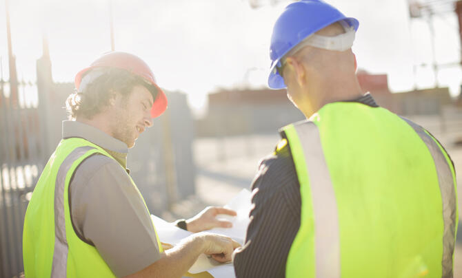 two workers with hard hats on reviewing a document