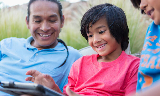 native american father and two sons looking at tablet sitting outside