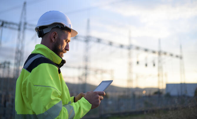 Engineer working on a tablet with substation and transmission line in background