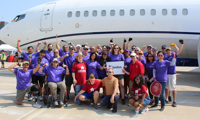 Leidos employees and volunteers from Special Olympics Virginia pose in front of an airplane at the 2022 Dulles Day Plan Pull. 