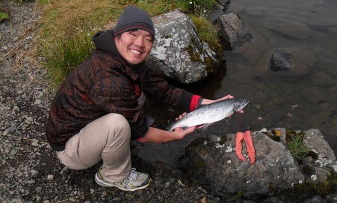 Adak tribe member holding salmon and smiling at camera