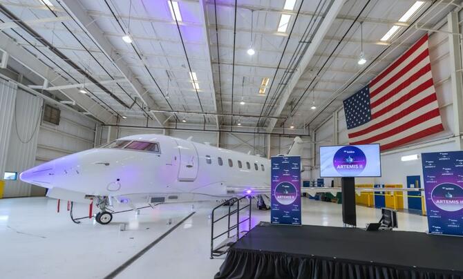 The Artemis II aircraft in a hanger with an American flag draped in the background