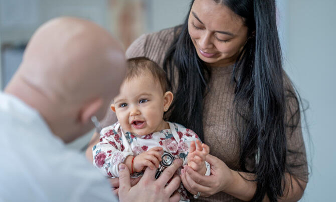 doctor listening to baby's heart while mother holds baby