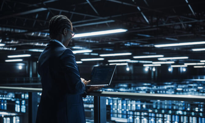 A woman standing at a computer facing a row of servers and computers