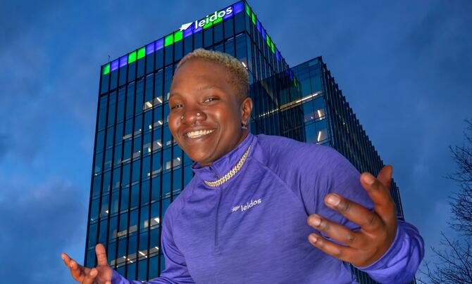Raven Saunders posing in a Leidos pullover in front of Leidos Global Headquarters. The building is lit up in green and purple.