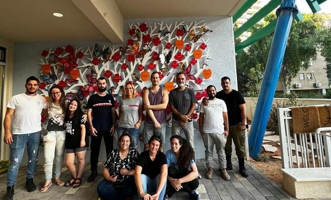Leidos Israel team posing for a group picture in front of a wall painted with flowers.