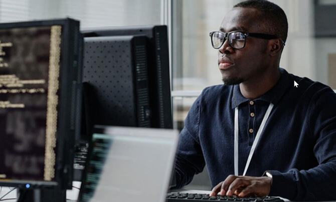 man working on computer with monitor displaying code