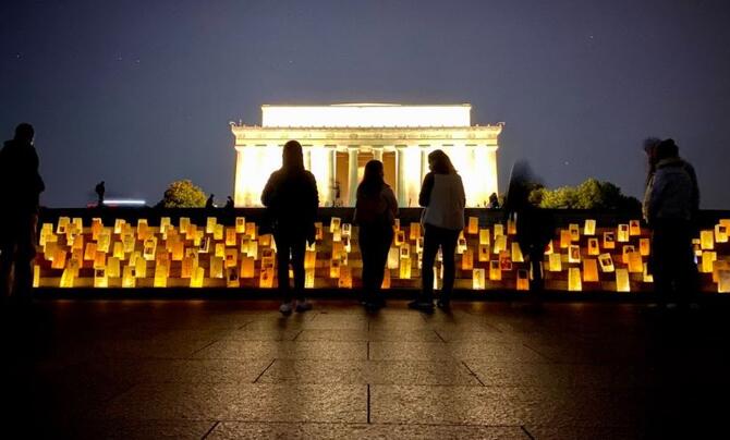 Volunteers stand over lanterns at the Lincoln Memorial at dusk