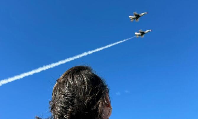 A Leidos employee looks up at the sky with two aircraft flying overhead 