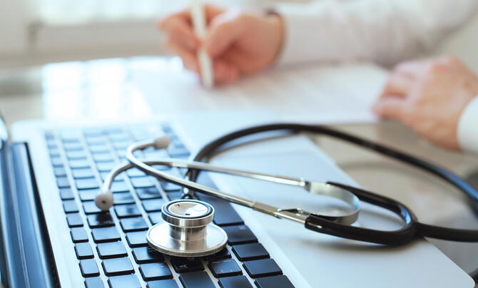Stethoscope on a laptop with a person writing in the background.