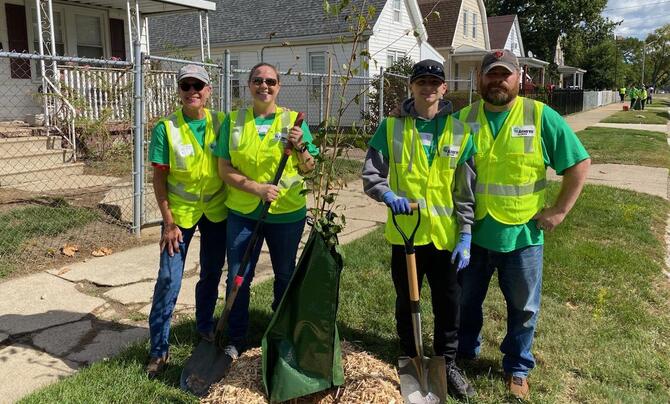 Four people stand next to a newly planted tree.