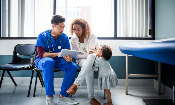 Male doctor showing digital tablet to mother by toddler in hospital