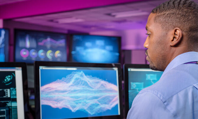 Man works in a computer center with multiple graphs displayed