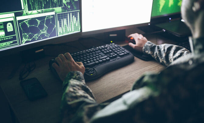 A soldier sits at a desk with a computer monitor and keyboard