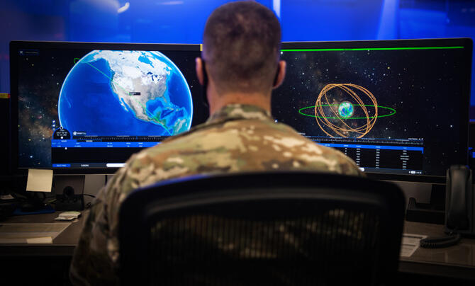 A man in uniform reviews data on two computer screens.