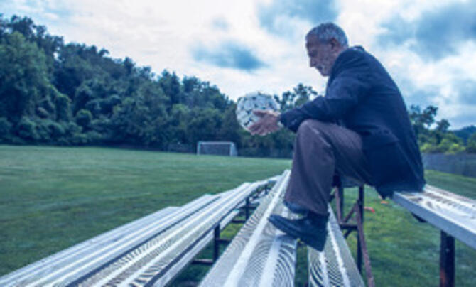 John Hindman sitting on bleachers holding a soccer ball