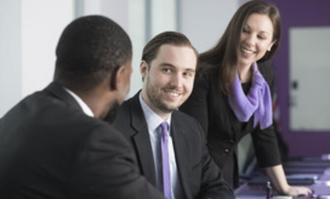 three people in a conference room chatting and smiling