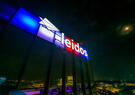 Leidos logo and wordmark pictured in a nighttime scene on top of Leidos GHQ lit up red white and blue