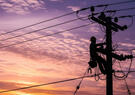 Lineman on a pole with sunset behind him