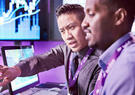 Two professionals review data on computer screens, with one pointing as they discuss.