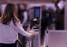 A traveler uses an automated airport eGate, scanning their passport at a self-service checkpoint with a biometric verification screen.