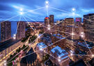 An aerial view of a city skyline at dusk features glowing location markers and connected lines overlaying the buildings, illustrating a digital network across an urban environment.