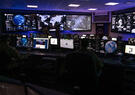 A security operations center with multiple large and small screens showing information, world maps