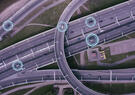 Aerial view of a highway interchange with digital overlays highlighting connected vehicles, illustrating intelligent transportation systems, real-time traffic monitoring, and vehicle-to-infrastructure communication.