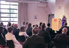Speaker addresses a seated audience during a professional event in a conference venue.