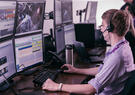 Leidos employee wearing a headset monitors multiple computer screens displaying operational data and video feeds.