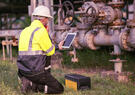 Engineer kneeling in front of pipes, holding a tablet.