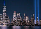 The illuminated New York City skyline at night, with the Tribute in Light beams rising into the sky beside Lower Manhattan.