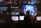A person facing away toward many screens showing the earth and the globe and other data