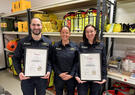 Two Leidos Australia Mission Aircrew holding Certificates, standing alongside Leidos RTO Compliance and Development Manager Nicole Powell