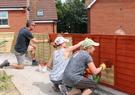 three people volunteering painting a fence