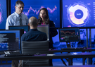 three coworkers discussing data on screens behind them