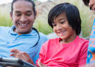 native american father and two sons looking at tablet sitting outside