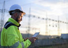 Engineer working on a tablet with substation and transmission line in background