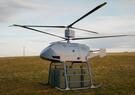 A small, helicopter-like uncrewed aerial system landed on a grassy field over an Army-green container.