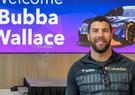 Bubba Wallace posing in front of a picture of his race car at Leidos Global Headquarters in Reston, Virginia