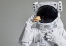 An astronaut wearing a pressurized space suit holding a sandwich