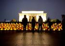 Volunteers stand over lanterns at the Lincoln Memorial at dusk