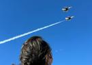 A Leidos employee looks up at the sky with two aircraft flying overhead 