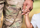 little girl holding hands with parent in military uniform