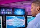 Man works in a computer center with multiple graphs displayed